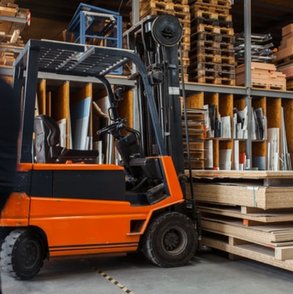An orange equipment lift holds wood in a storage facility