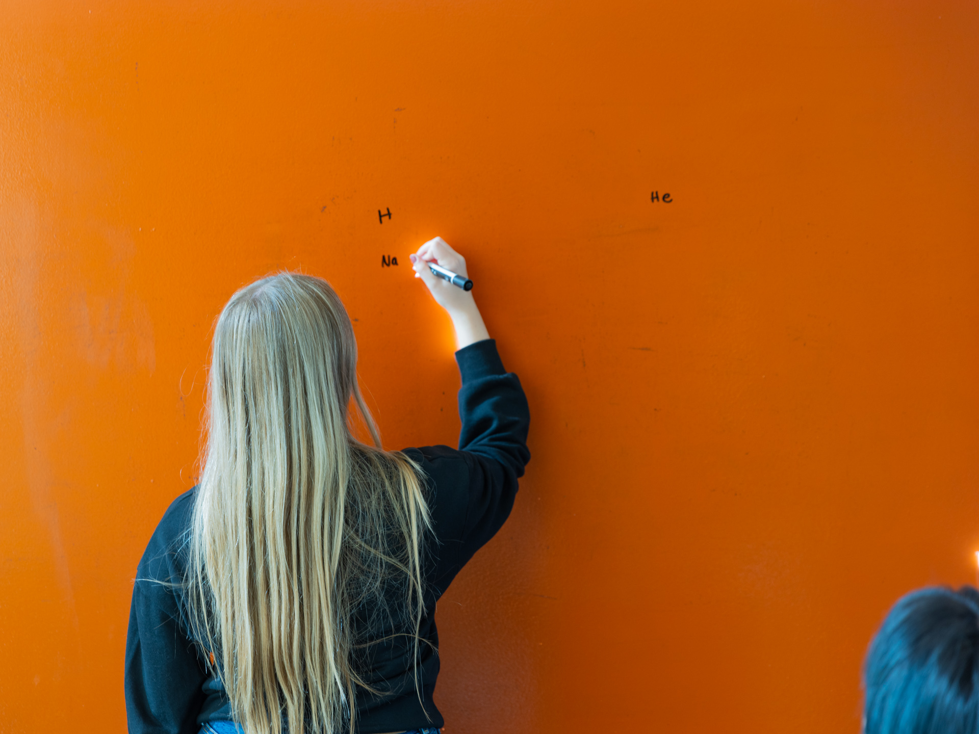 Shot of a blonde woman from behind writing on an orange wall thanks to business development services in Lawrence